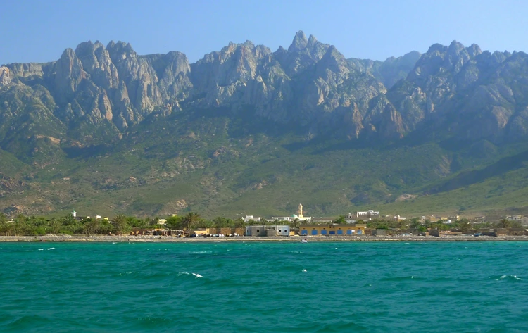 a small coastal village with mountains in the background.